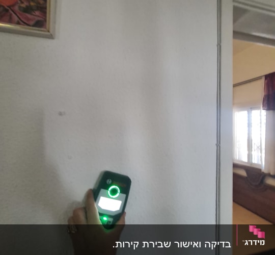 יד מחזיקה מכשיר מדידה על קיר לבן